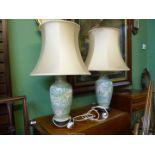 A pair of Oriental style lamps in muted green, blue and pink water lily design having peach shades.