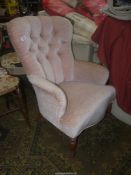 A pink/peach coloured upholstered buttonback Chair standing on turned front legs.