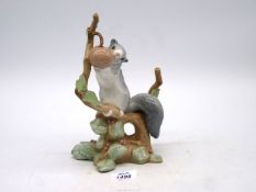 A Lladro figure of a grey squirrel on a branch eating a berry, 9" tall.