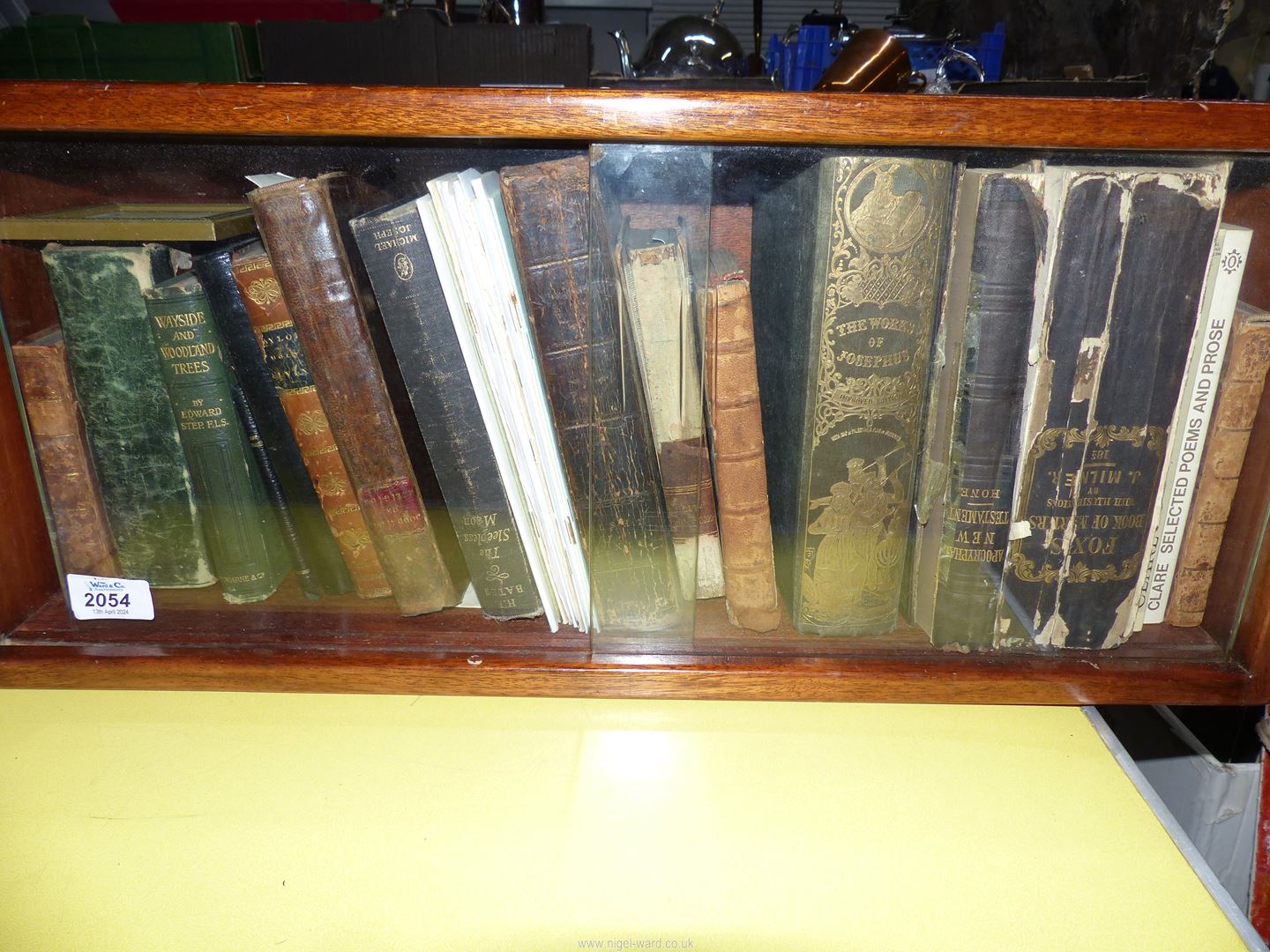 A small wooden bookcase with glass doors containing books to include Wayside and Woodland Trees,