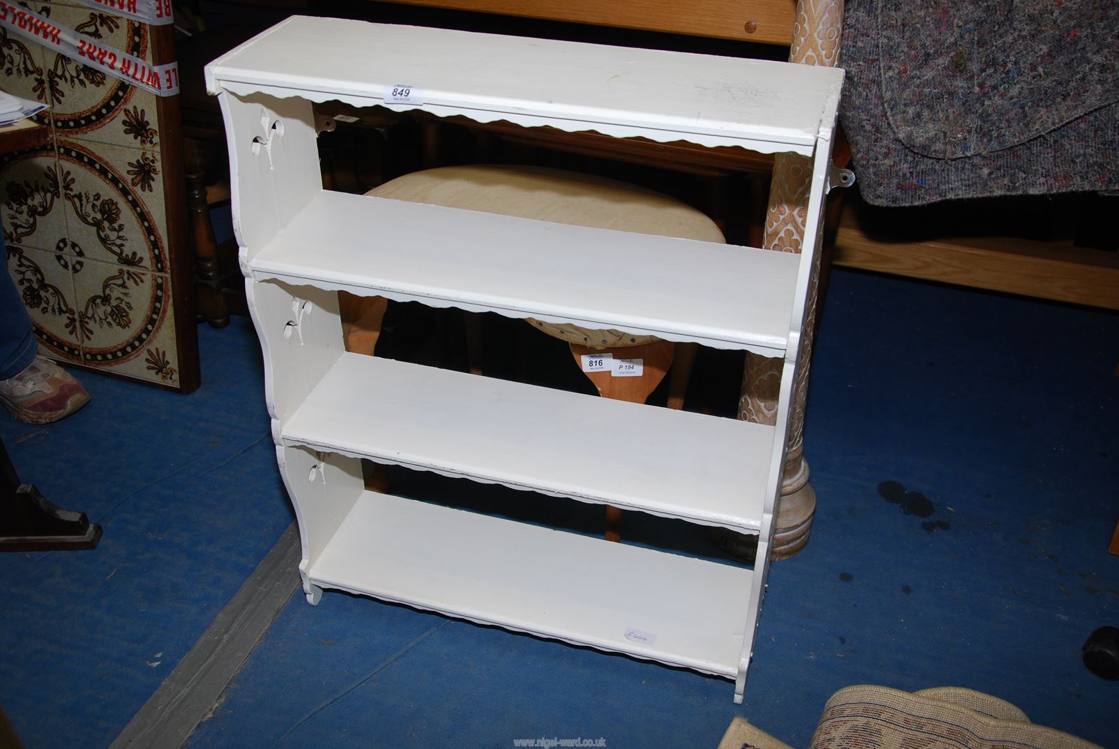 A white painted wall shelf unit having four scalloped edge shelves.