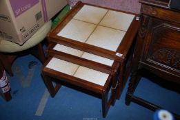 A nest of three teak framed tables having a tiled top.