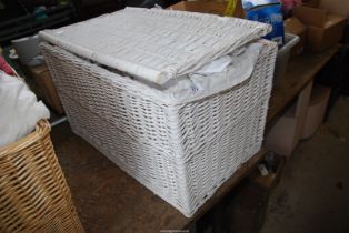 A large wicker linen basket with sheets, bedspread, pillows, bed throw etc.