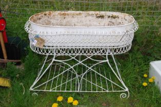 A wire and metal planter on a stand, possibly originally a child's cradle.