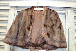 A short fur cape with brown lining, elasticated stay across back.