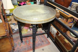 An early 20th century Benares brass top table with hammered design, on folding wooden base,