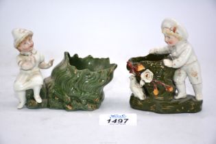 Two small ornaments of young children beside green tree trunk/vases;