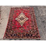 A border patterned and fringed rug in vibrant red ground having a central cream medallion and a
