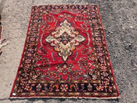A border patterned and fringed rug in vibrant red ground having a central cream medallion and a