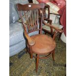 A hardwood framed Arts and Crafts circular seated Elbow Chair having a six turned stick back,
