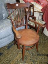 A hardwood framed Arts and Crafts circular seated Elbow Chair having a six turned stick back,