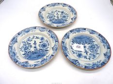 Three blue and white Delft plates with fence and floral decorations and a terracotta colour rim.