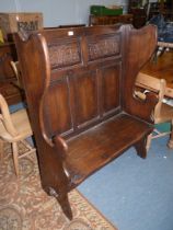 A peg-joyned Oak Settle having a pair of carved panels to the backrest with arch and stylised