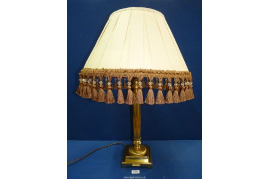 A brass column lamp with large cream shade having gold coloured tassels.