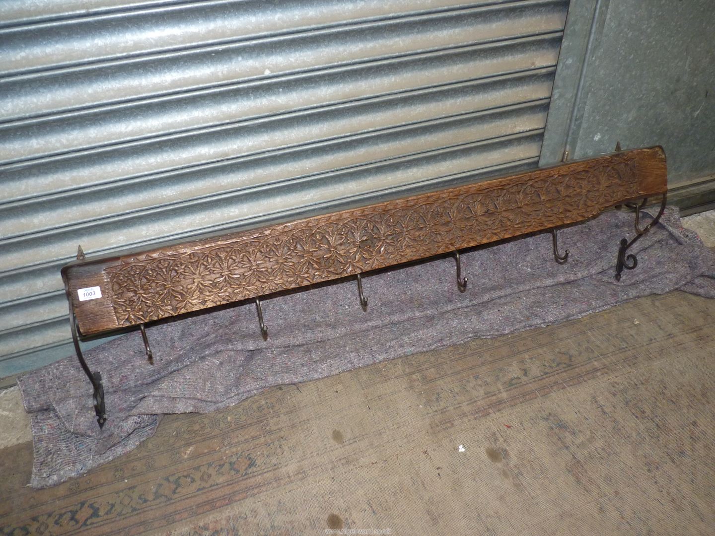 A rustic Indian carved wall shelf/coat rack, having wrought iron scroll work wall fixings, 55" long.