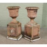 A pair of terracotta garden urns raised on plinths. Height 82.5cm.