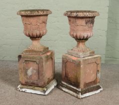 A pair of terracotta garden urns raised on plinths. Height 82.5cm.