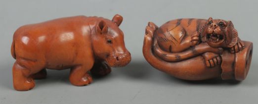 Two carved hardwood netsukes, in the forms of a hippopotamus and a tiger in the palm of a hand. Both