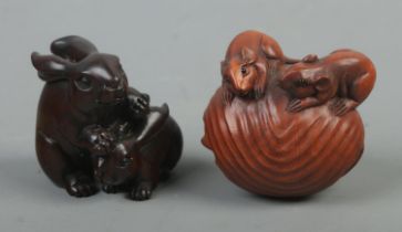 Two carved hardwood netsukes, depicting two rabbits and three mice within a nutshell. Both signed.
