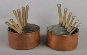 Two sets of six graduated copper pans, with brass handles.