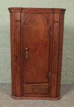 An early Victorian oak hanging corner cupboard with cupboard door over singular drawer flanked by