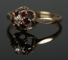 A 9ct gold cluster ring set with six garnets surrounding a central diamond. Size Q, 1.8g.