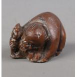 A Japanese carved hardwood netsuke formed as crouching elder holding a staff.