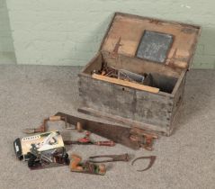A wooden twin handled tool chest with contents. Includes saws, door handles, Radius Ltd stove,