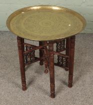 An Eastern brass top table with decorative turned wooden base.