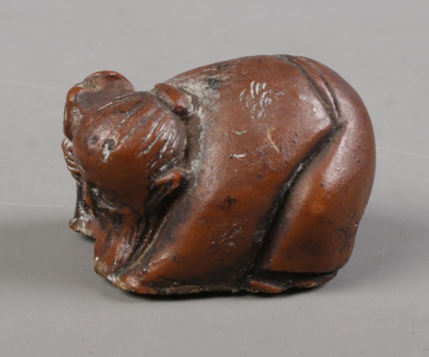 A Japanese carved hardwood netsuke formed as crouching elder holding a staff. - Image 2 of 2