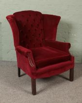 A wing back arm chair with button back and red velvet upholstery.