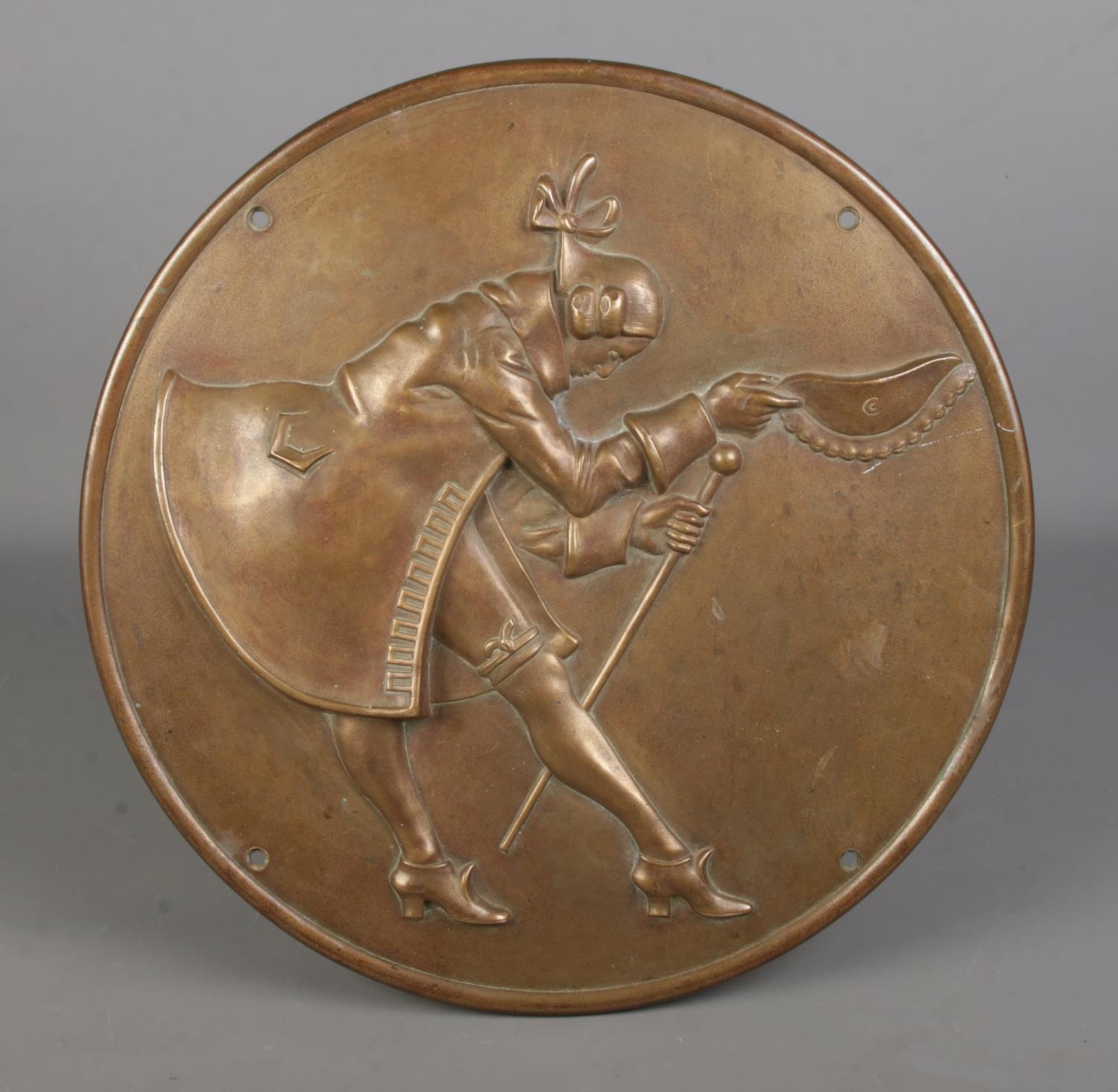 A large circular bronze plaque, depicting a gentleman holding a cane doffing his hat. Diameter: