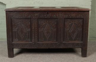 An 18th century oak joined coffer with hinged top and profusely carved tri panel base fitted with