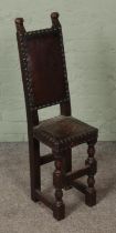 An oak child's narrow correction chair featuring studded leather back and seat with turned supports.