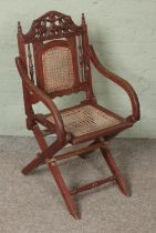 A campaign style folding armchair featuring carved insignia. With bergere seat base and back rest.