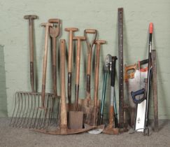 A collection of assorted tools to include spades, rakes, pickaxe, sledgehammer, saws, etc.