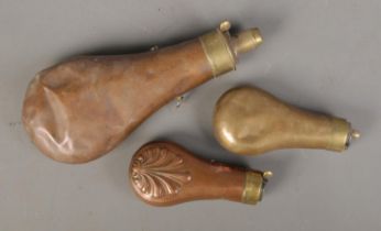 Three copper powder flasks including example featuring shell pattern decoration.