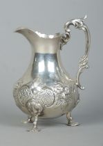 A Victorian silver cream jug with repousse decoration, scrolling handle and raised on three hoof