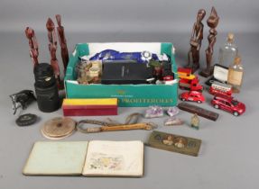 A box of collectables. Includes wooden tribal figures, pens, diecast vehicles, chemist bottles,