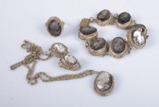 A white metal shell cameo jewellery suite featuring bracelet, ring, earrings and necklace. Makers