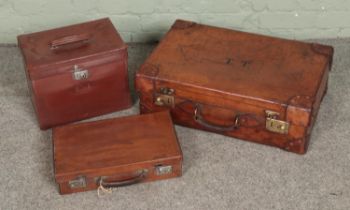 Three vintage leather suitcases of varying sizes with two monogramed to fronts.