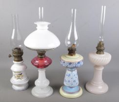 A collection of four oil lamps, examples having chintzy blue flowers and opaque glass designs.