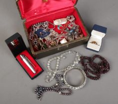 A case of costume jewellery. Includes garnet necklace, pearl necklace, pipe lighter, enamelled