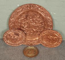 A large embossed copper wall plate along with two smaller examples and a brass example. Largest 72cm