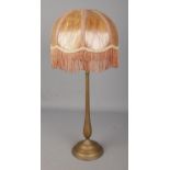 A brass rise and fall table lamp in the style of Benson with fringed shade.
