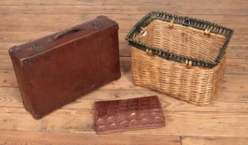 A wicker basket containing an early 20th century crocodile skin clutch bag and a vintage suitcase.
