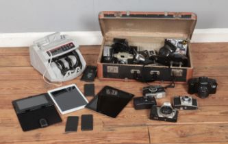 A vintage suitcase containing a variety of cameras and equipment along with bill counter and small