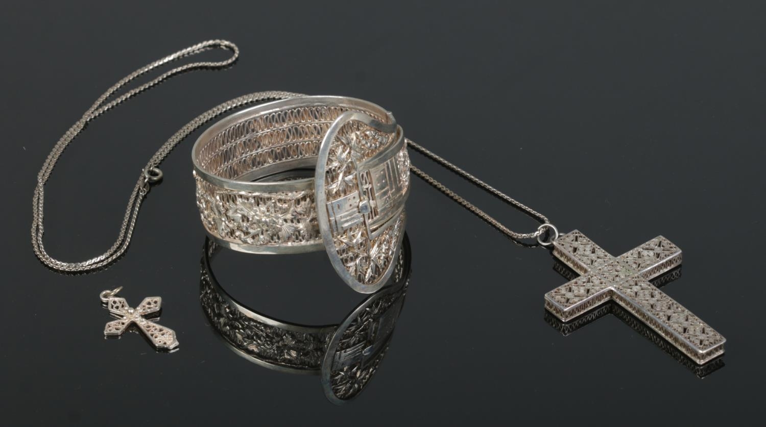 Three pieces of white metal filigree/wirework jewellery, to include hinged bangle, large crucifix