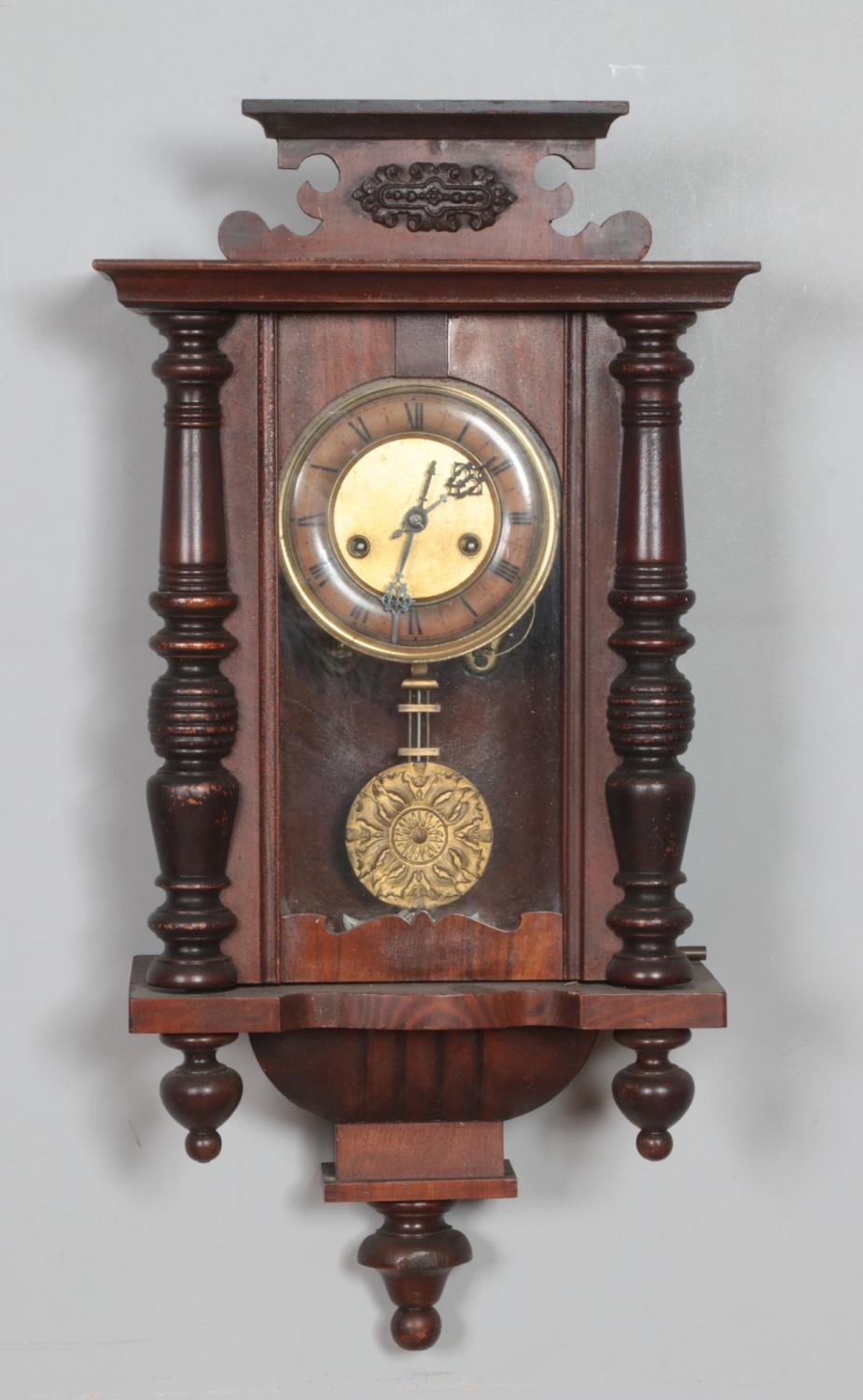 A mahogany cased wall clock with turned supports and carved detail.