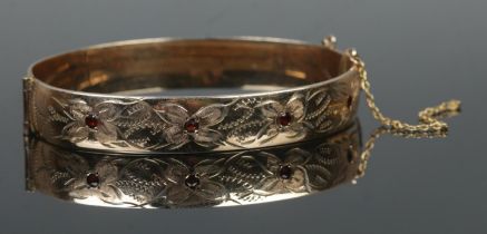 A 9ct rolled gold hinged bangle, set with four garnet stones and half engraved detailing. Safety